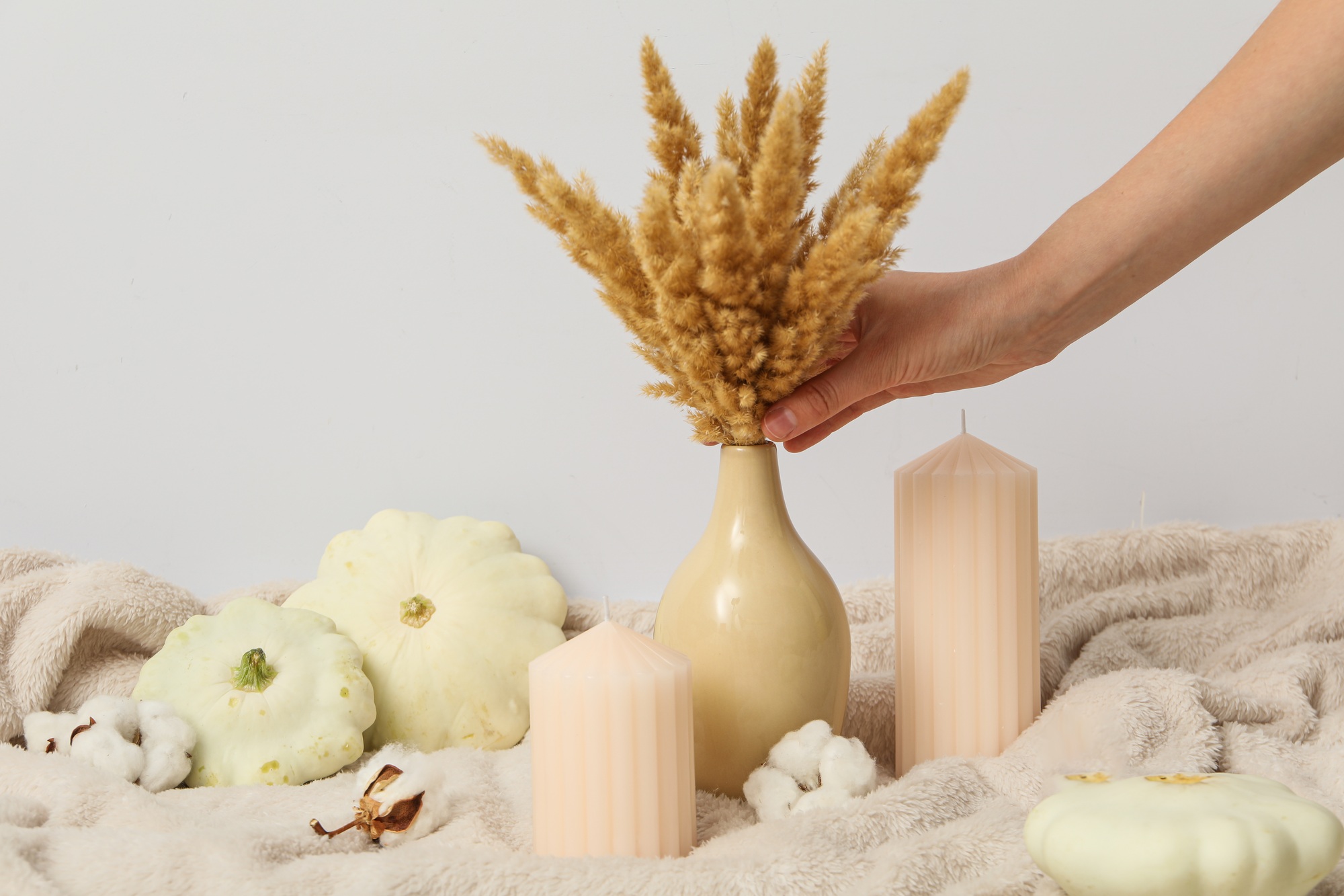 Candles, bouquet in female hand and zucchini on beige background